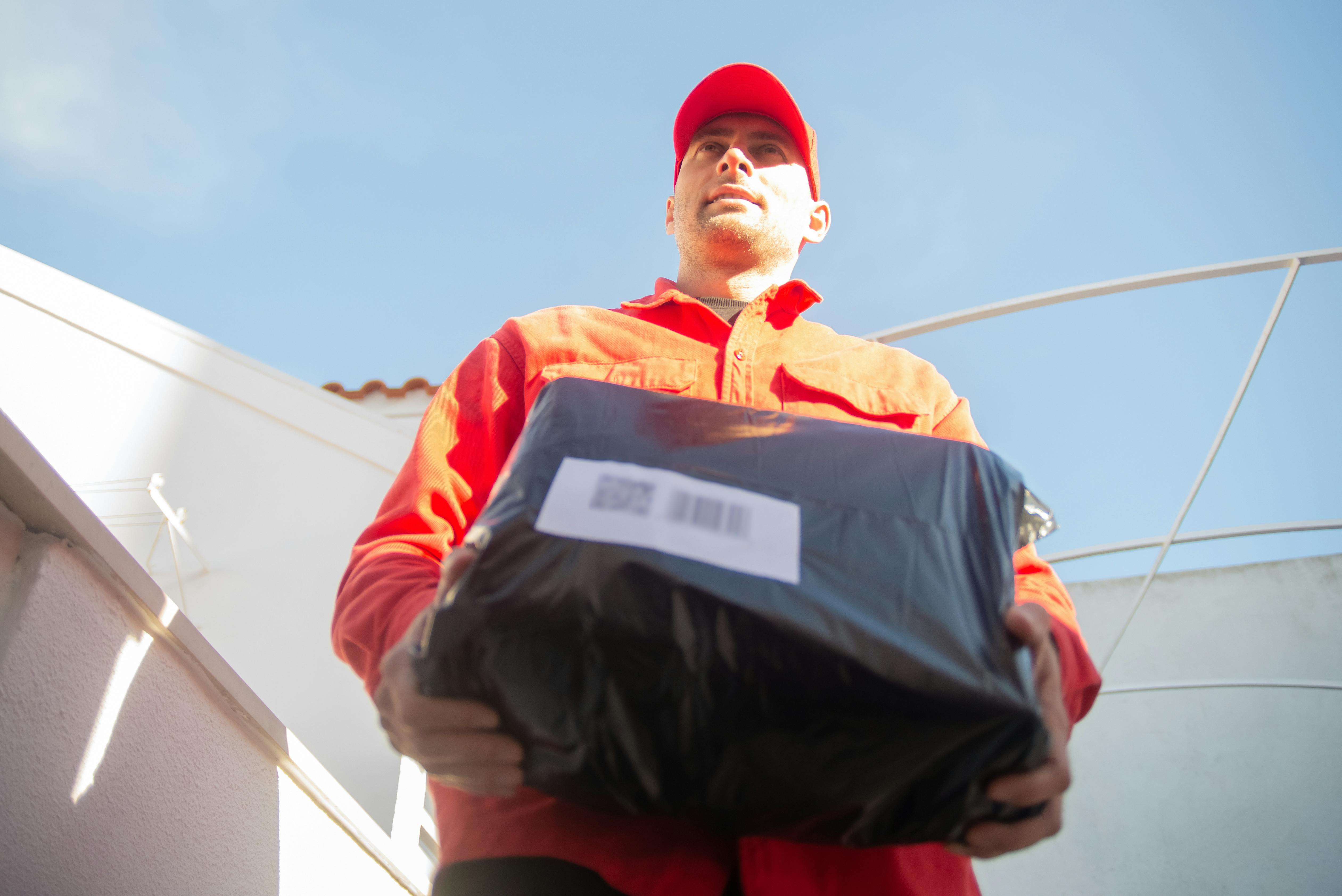 Courier in red uniform holding a packaged order during delivery handoff.